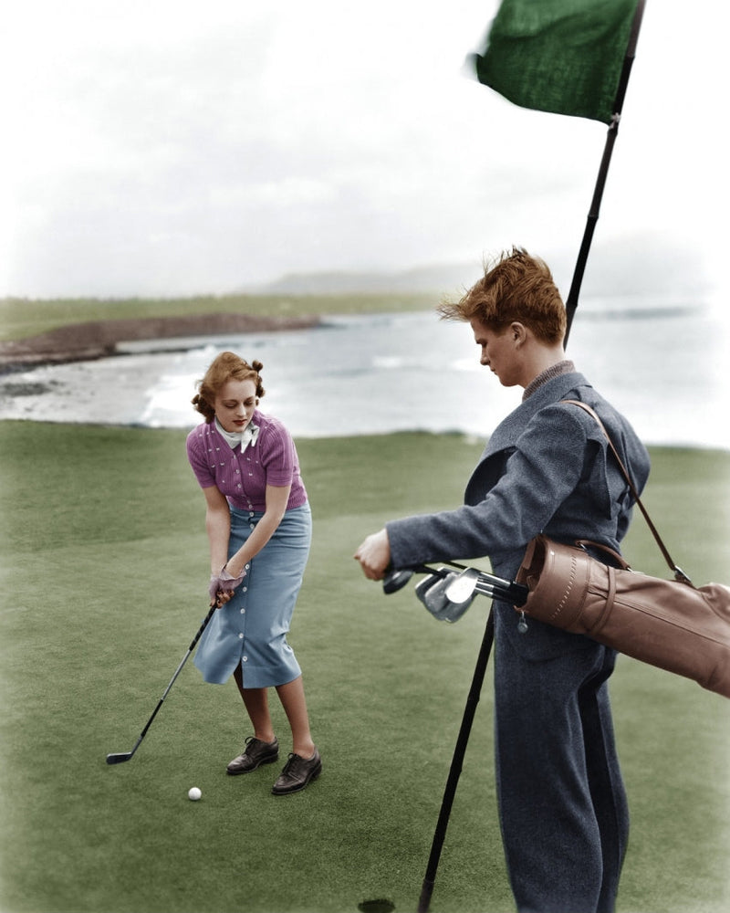 A old picture of a female golfer and a caddie.