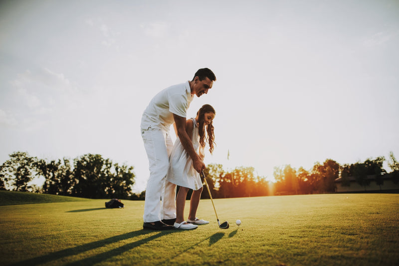 Father directs and teaches the girl how to play golf.