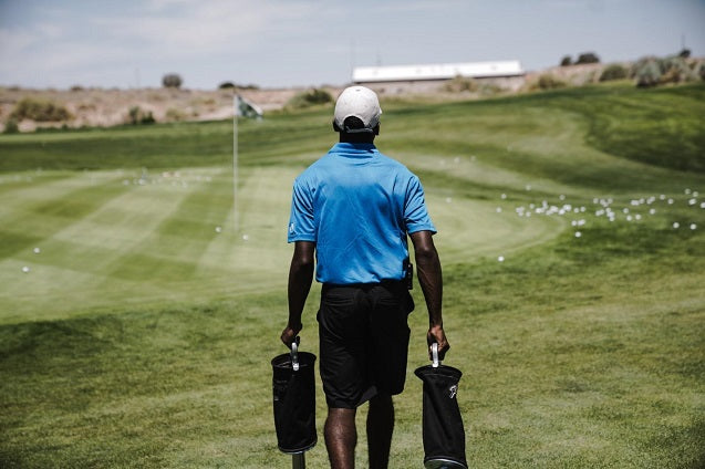 man walking on the golf course carrying bags