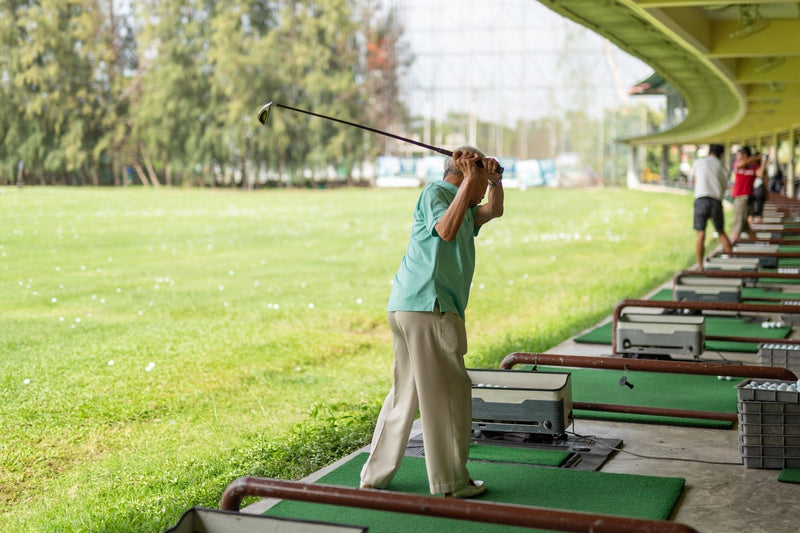old man swinging club at golf ball at driving range