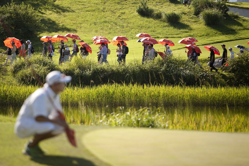 People in a golf field with red and white umbrellas