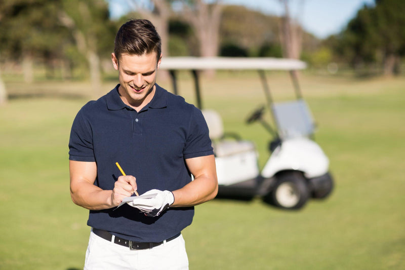 Smiling golfer writing on score card while standing at golf course