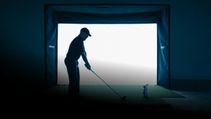 Silhouette of a golfer practicing indoors with a bright light source behind him.