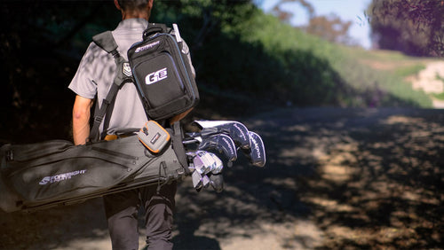 A man walking down a dirt trail carrying a golf bag