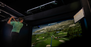 Man golfing indoors with golf simulator